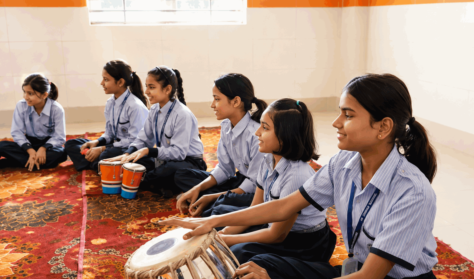Students sitting on the floor playing tabla and other instruments in the music room